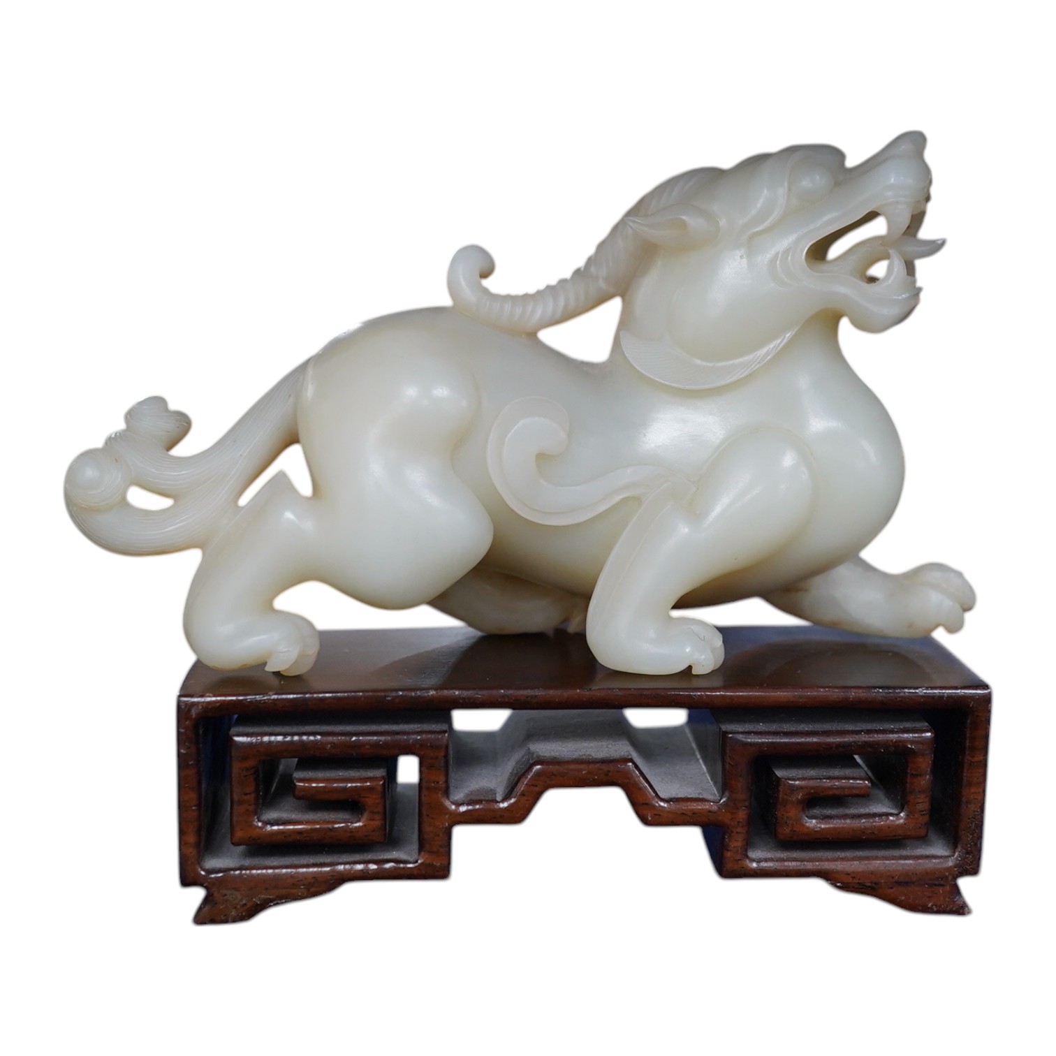 A large Chinese archaistic white jade figure of a mythical beast, hardwood stand, 9cm high, 16cm wide. Condition - good.